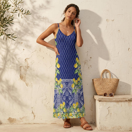 May include: A blue maxi dress with a white geometric pattern and lemon print. The dress has spaghetti straps and a V-neck. A straw tote bag and sunglasses sit on a stone bench.