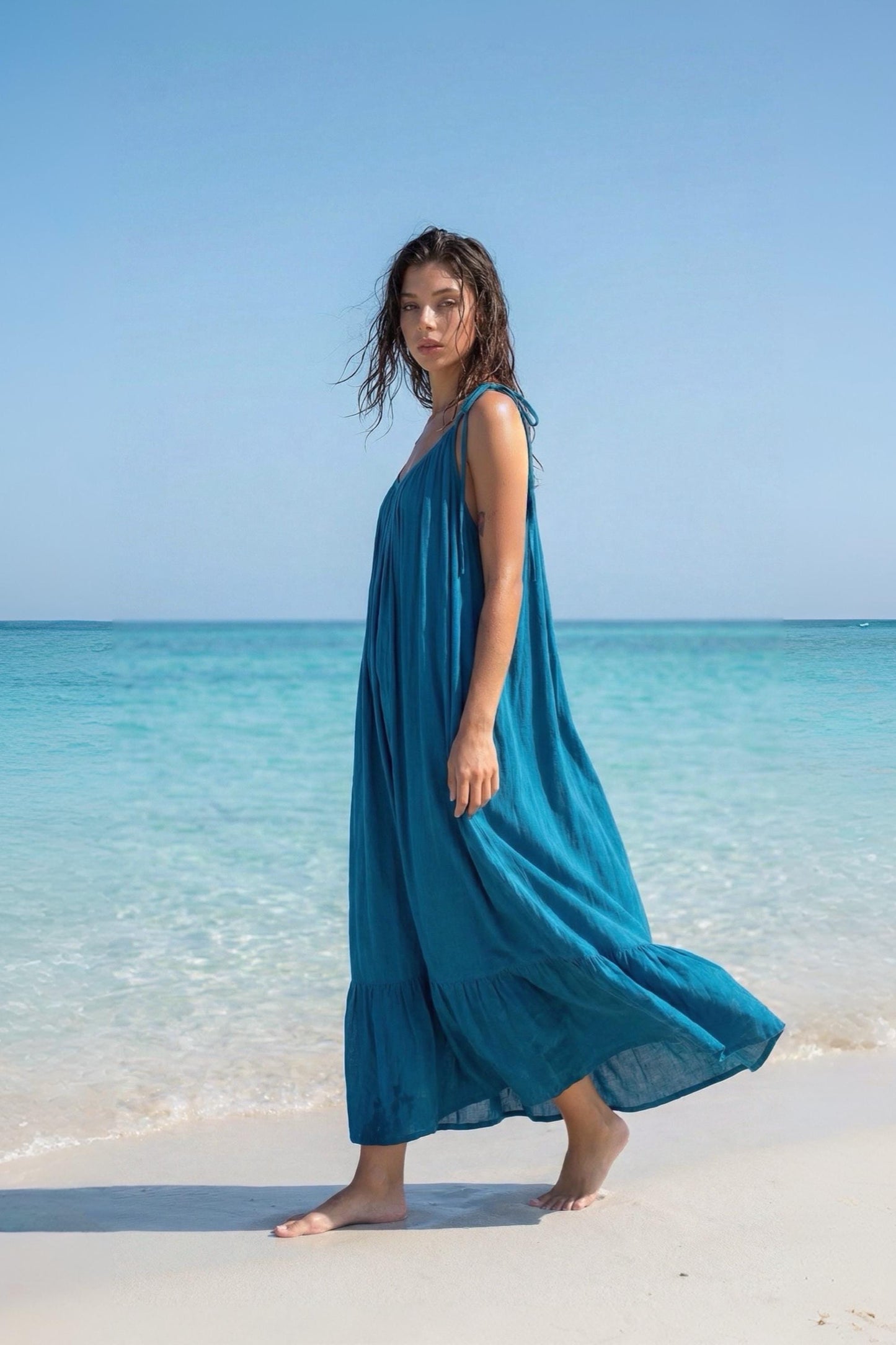 Side view of a blue turquoise maxi dress with open back, tie shoulders, and ruffle hem, styled as a flowy beach and resort dress.