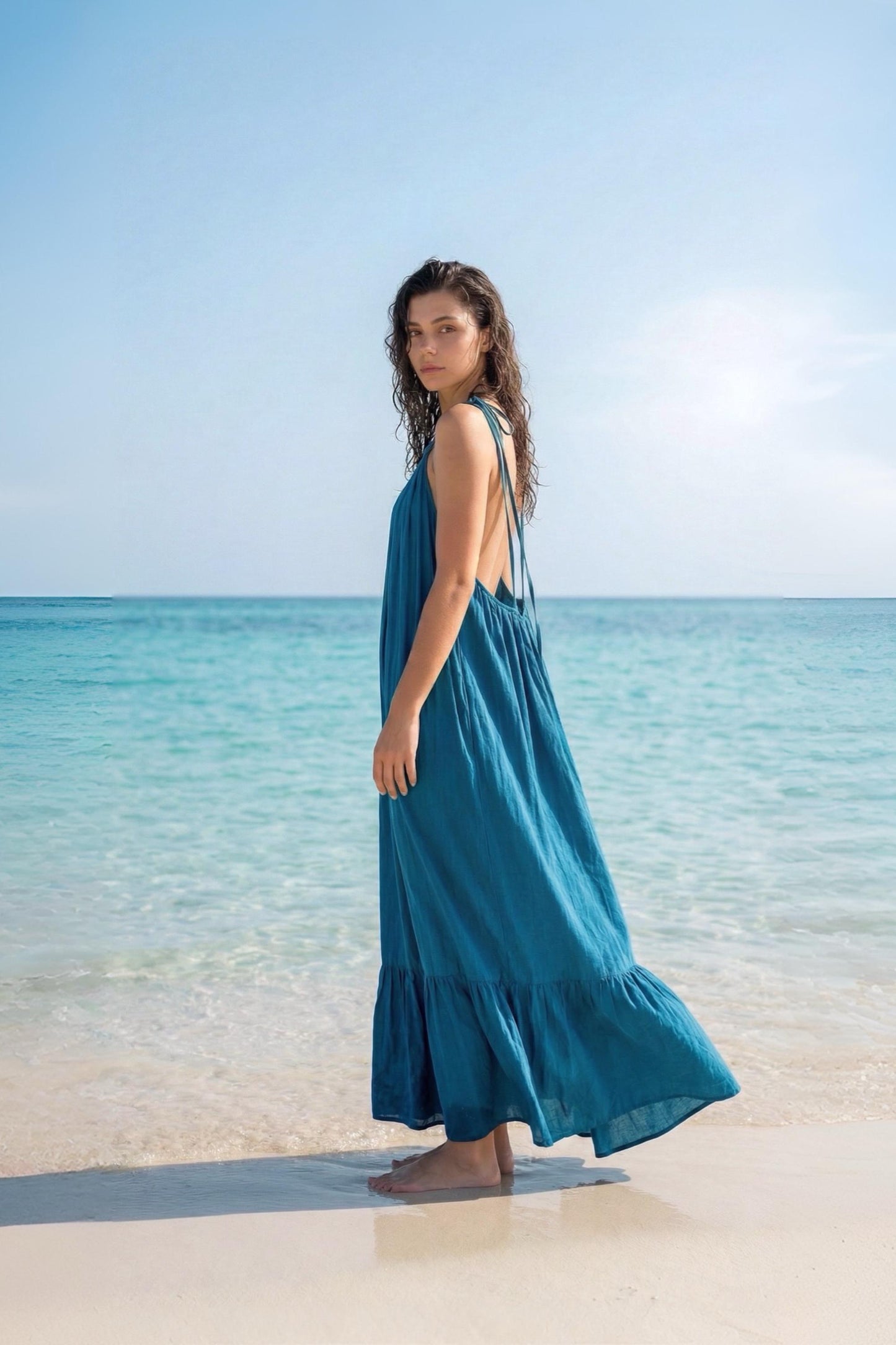 Side view of a blue turquoise maxi dress with open back, tie shoulders, and ruffle hem, styled as a flowy beach and resort dress.