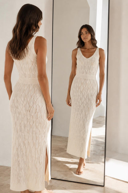 May include: A sleeveless cream-colored midi dress featuring a textured knit pattern with vertical leaf-like motifs, a V-neckline, a fitted waist section, and a side slit along the lower hem, shown from both a back and front perspective in a mirror.