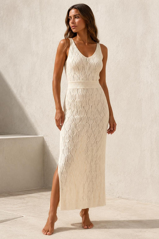 May include: A sleeveless cream-colored midi dress featuring an intricate openwork knit pattern with a vertical leaf-like design, a V-neckline, a fitted waist section, and a straight skirt with a side slit that extends to the mid-thigh area.