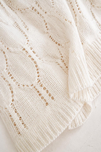 May include: A cream-colored knit sweater featuring an intricate openwork diamond pattern. The garment displays a vertical ribbed texture along the edges and a soft, textured weave throughout, showcasing a detailed cable-knit design with small holes.