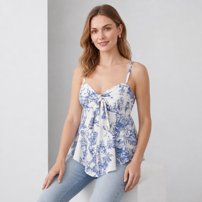 May include: A white sleeveless top featuring a blue toile de jouy pattern, a sweetheart neckline, thin shoulder straps, and a central tie-front detail that creates a gathered effect above a slightly flared hemline, paired with light blue denim jeans.