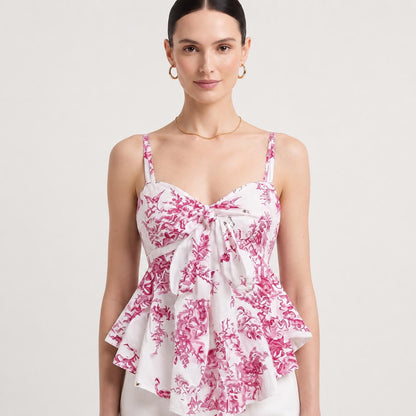 May include: A white sleeveless peplum top featuring a vibrant magenta toile de jouy pattern. The garment has thin shoulder straps, a sweetheart neckline, and a prominent fabric tie detail at the center front that creates a draped, layered effect.