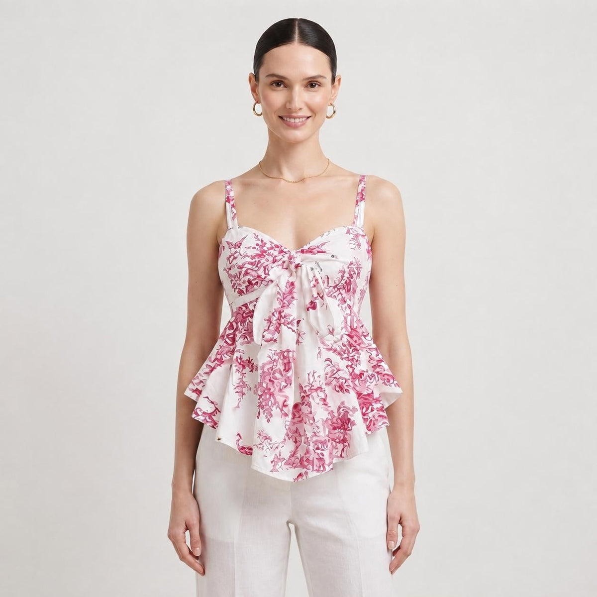 May include: A sleeveless white camisole top featuring a vibrant magenta floral toile pattern, thin shoulder straps, a sweetheart neckline, and a central tie-front detail that creates a flared, peplum-style silhouette at the waistline.