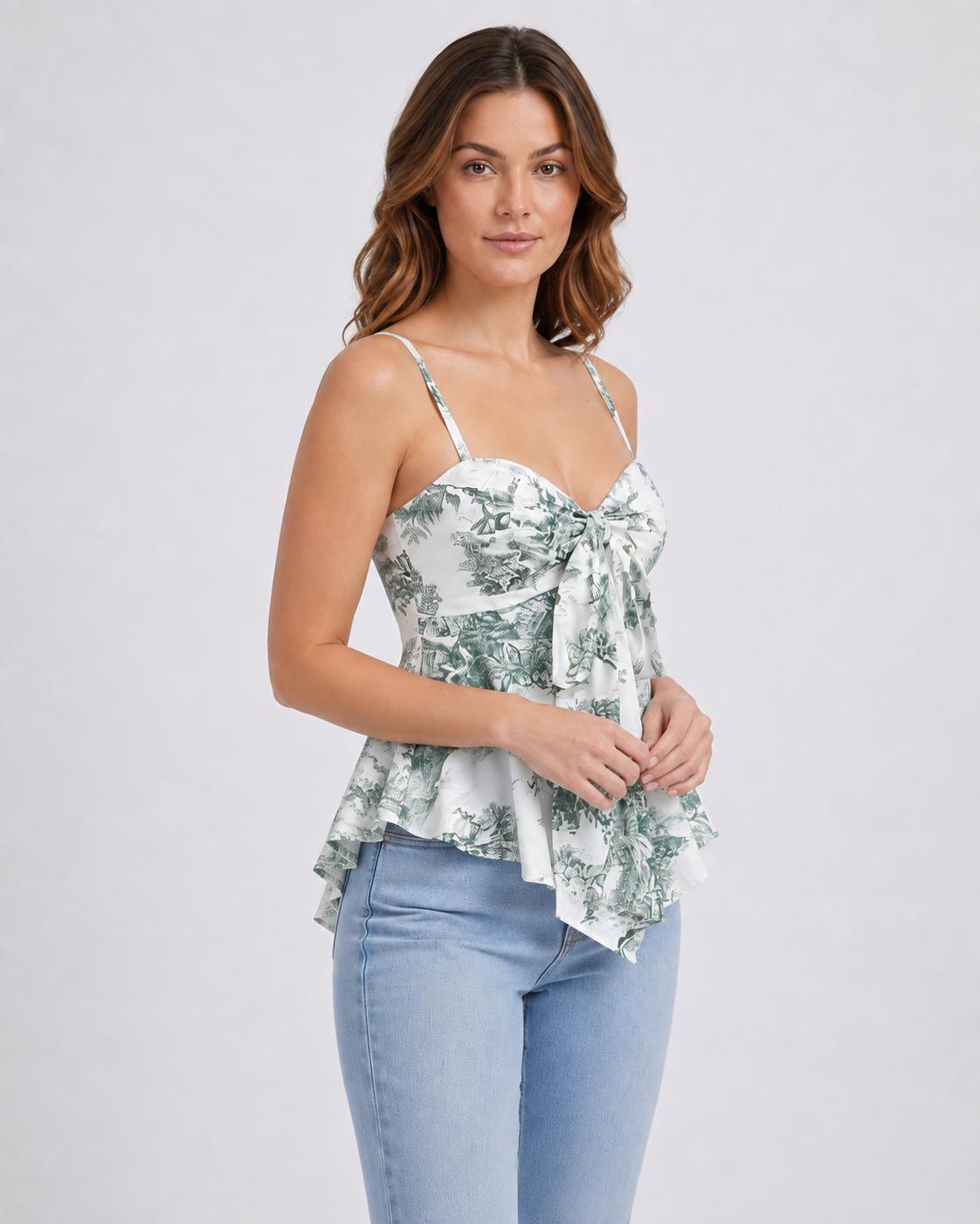 May include: A sleeveless white top featuring a green toile de jouy print, thin spaghetti straps, a sweetheart neckline, and a front tie detail. The bodice is fitted with a flared, asymmetrical hemline that falls below the waistline.